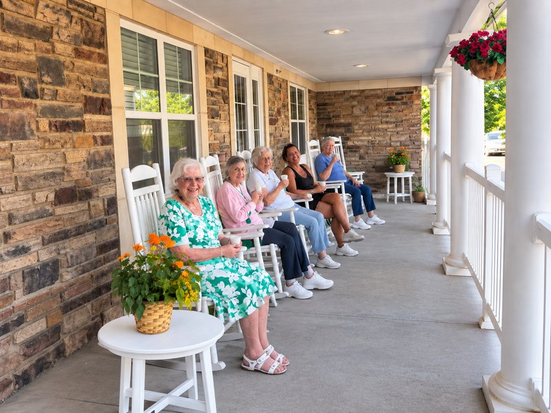 Senior living residents relaxing in rocking chairs on the community's covered front porch.