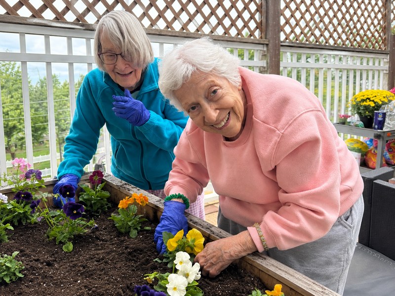 Assisted living residents potting flowers together during an outdoor garden club meeting.