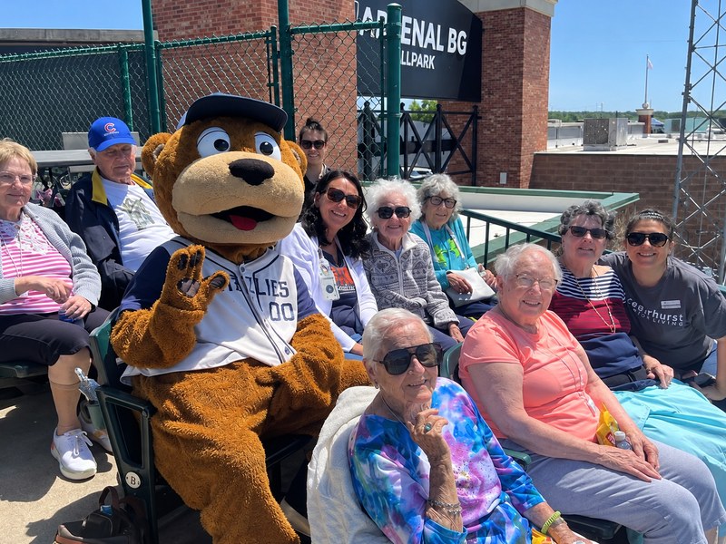 Senior living residents and team members posing with the team mascot at a Gateway Grizzlies baseball game.