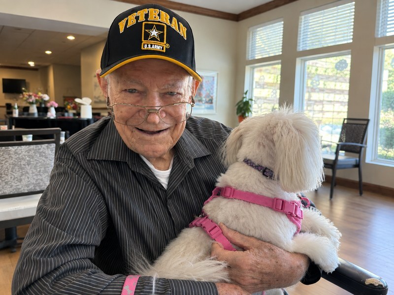 Senior living community resident and U.S. Army veteran smiling while holding his small white dog.