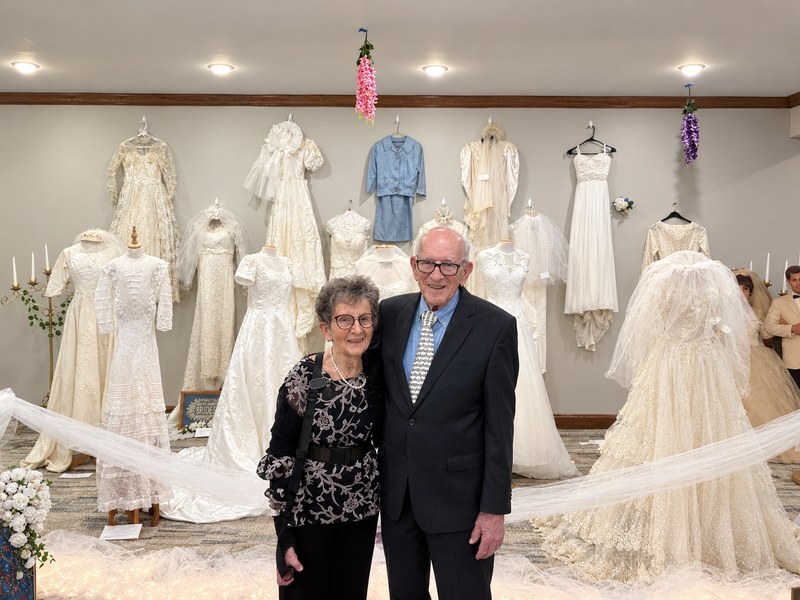 Senior living residents standing in front of a display of vintage wedding gowns.