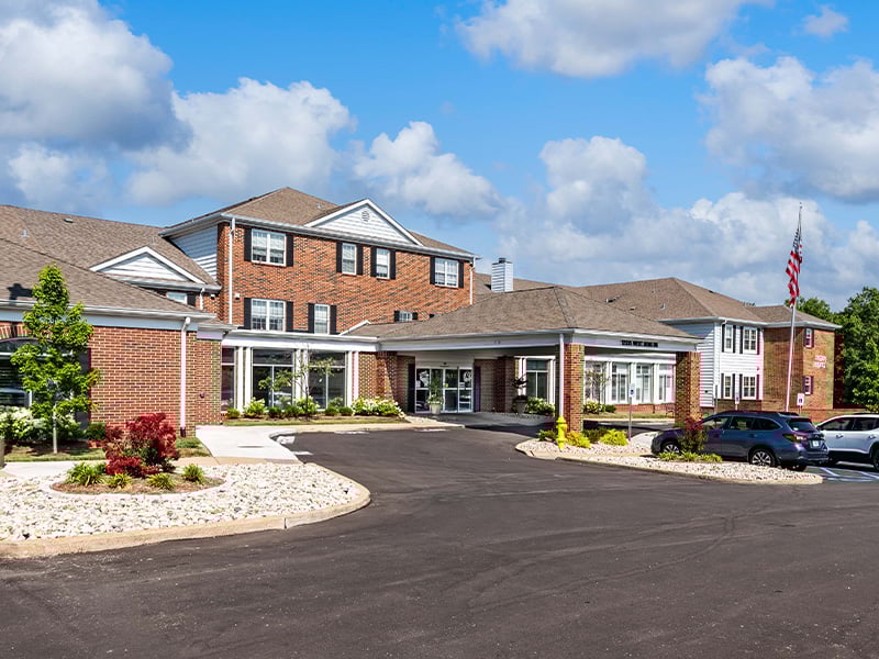 An inviting view of the Cedarhurst of Tesson Heights senior living community from the outside, complete with the main building and its distinctive sign