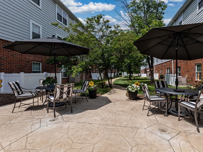 Outdoor green space at Cedarhurst of Tesson Heights with paved walking paths and comfortable, shaded seating