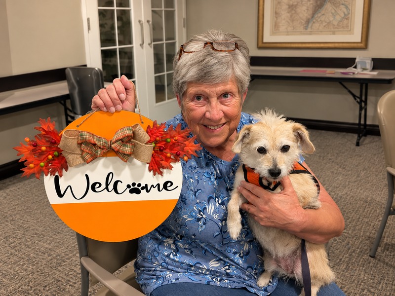 Assisted living resident holding a handmade welcome sign and her small dog at pet-friendly Cedarhurst of Tesson Heights