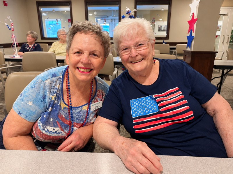 Two friends smiling side by side at a community celebration at Cedarhurst of Tesson Heights senior living community