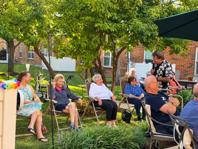 Residents enjoying live entertainment in a shaded courtyard at Cedarhurst of Tesson Heights senior living community