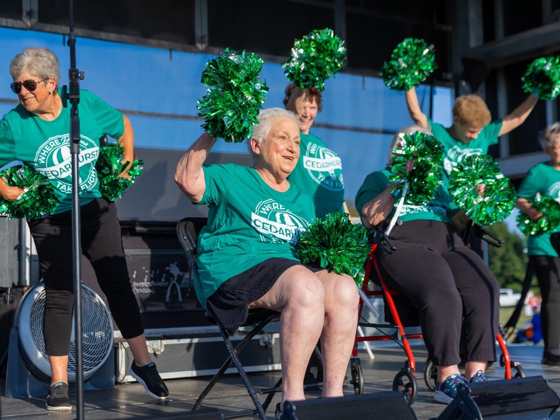 Residents of Cedarhurst of Tesson Heights assisted living community performing a pom pom routine on stage