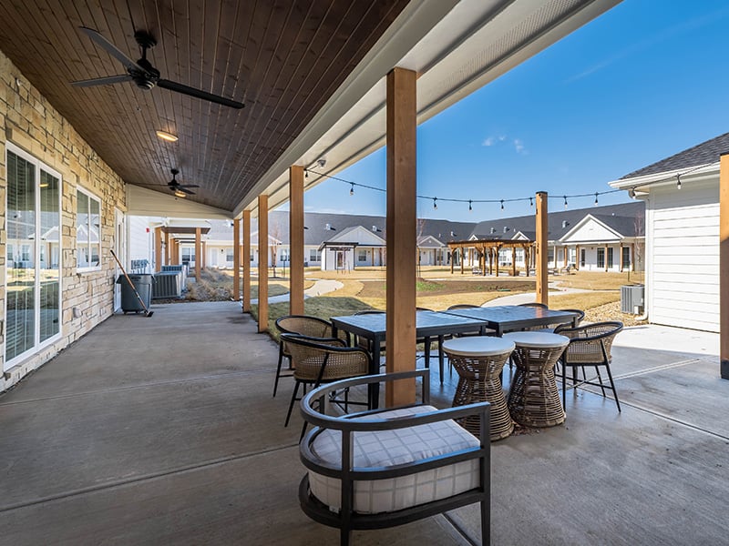 An inviting outdoor area at Cedarhurst of Topeka, showing lush green spaces, paved paths, comfortable seating, a pergola, and a covered patio