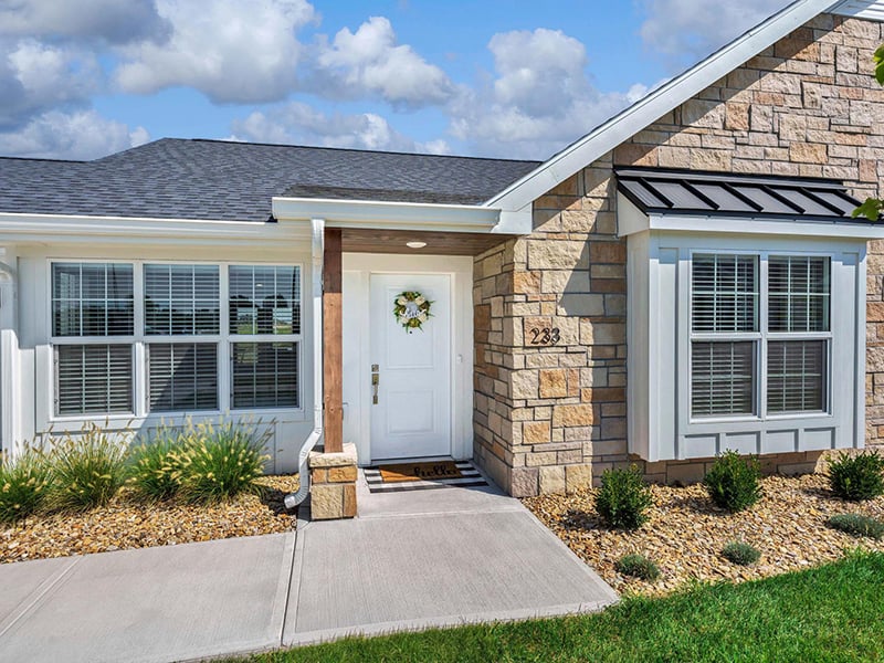 A Cedarhurst of Topeka Independent Living at Cedarhurst Cottages unit exterior featuring a stone facade, covered front porch, and landscaped entryway.