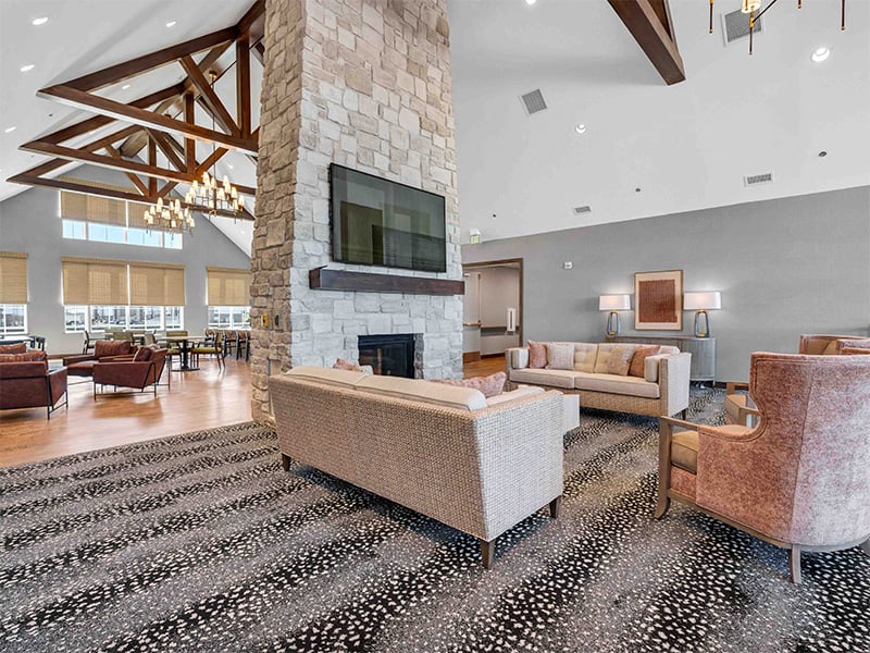 A spacious and inviting common area at Cedarhurst of Wentzville, designed for connection with comfortable seating, a cozy fireplace, and a television for residents across all living options
