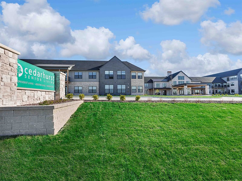 An inviting view of the Cedarhurst of Wentzville senior living community from the outside, complete with the main building and its distinctive sign