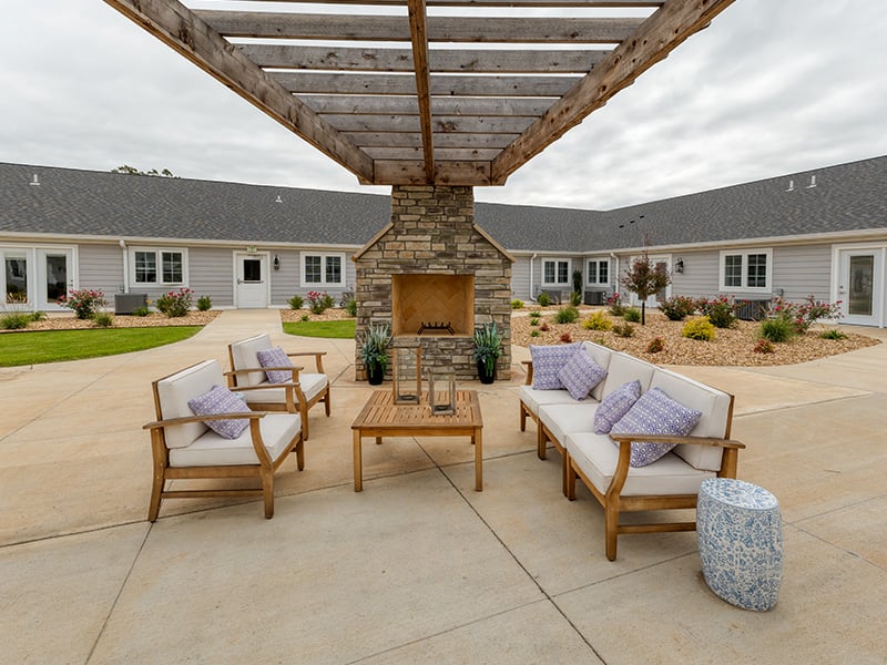 An inviting outdoor patio space with a wooden pergola with fireplace at Cedarhurst of West Plains senior living community.