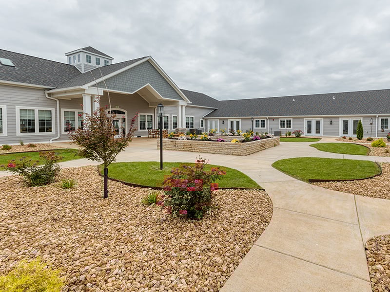 Outdoor green space at Cedarhurst of West Plains with paved walking paths and raised garden beds.