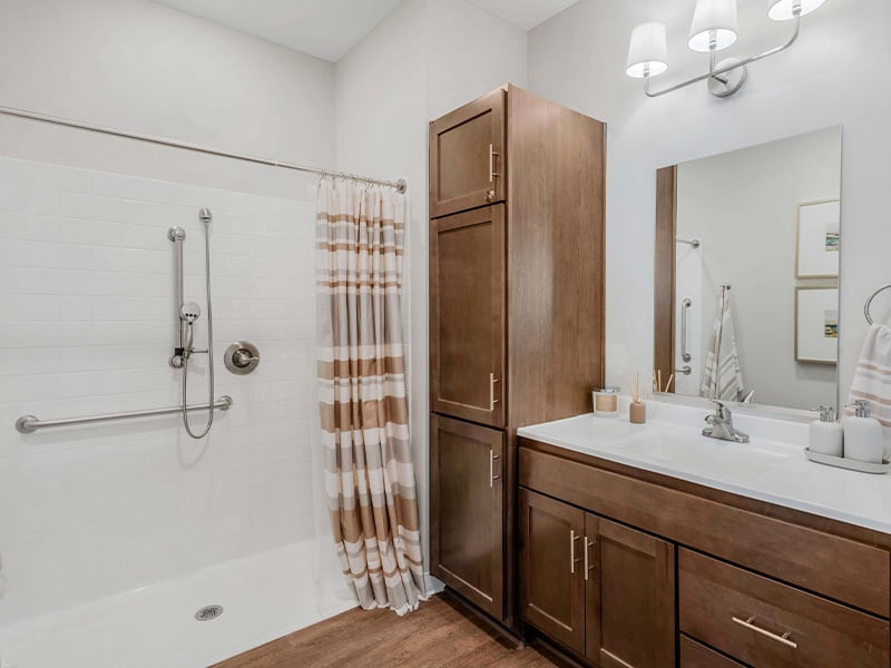 An accessible bathroom in a senior apartment at Cedarhurst of Wichita, featuring safety rails and a roll-in shower