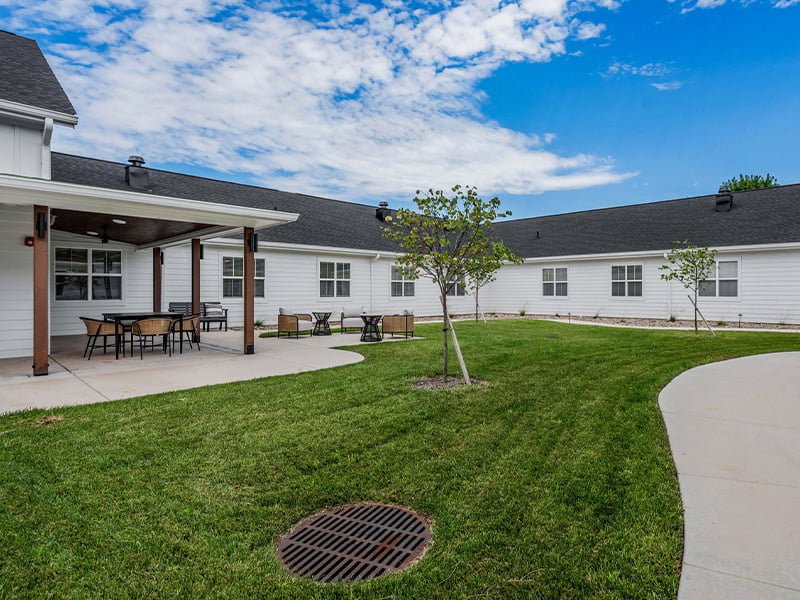 An inviting outdoor area at Cedarhurst of Wichita, showing lush green spaces, paved paths, comfortable seating, and a covered patio