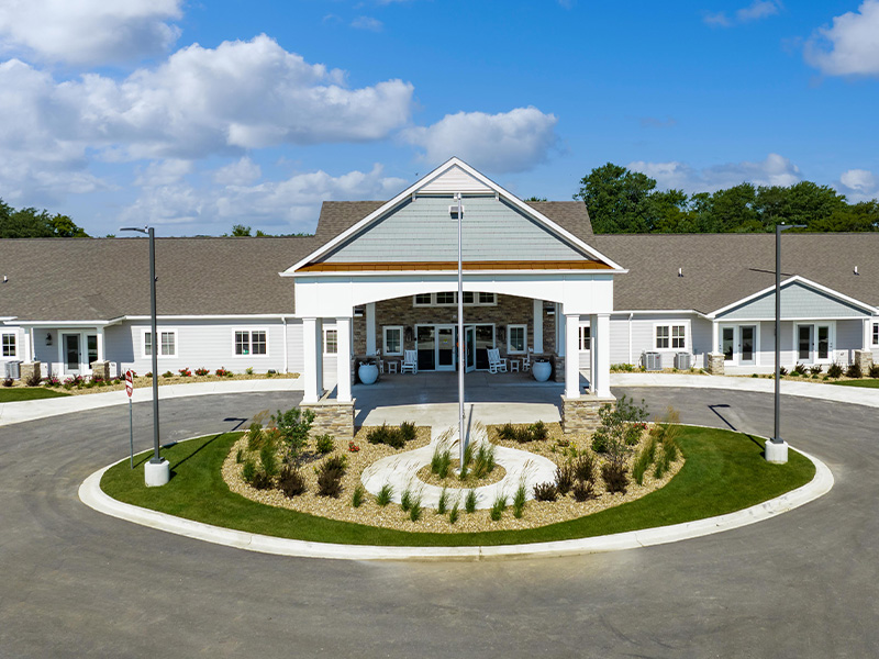 An inviting view of the Cedarhurst of Woodstock  senior living community from the outside, complete with the main building and its distinctive sign