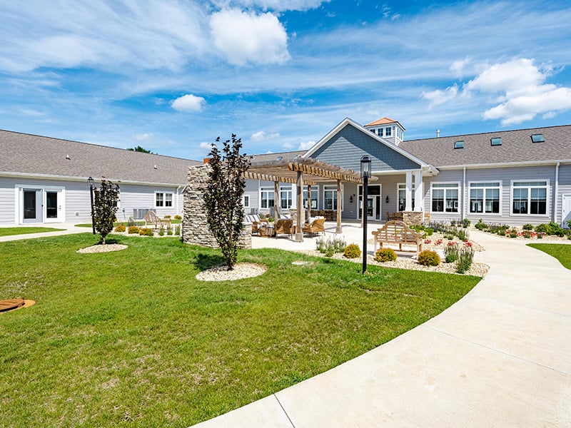 An inviting outdoor area at Cedarhurst of Woodstock, showing lush green spaces, paved paths, comfortable seating, and a pergola
