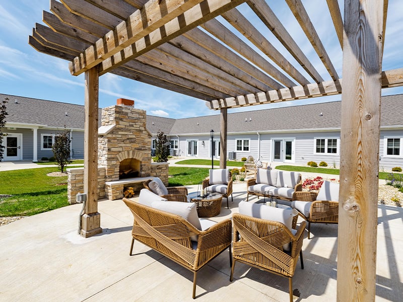 An inviting outdoor patio space with a wooden pergola with fireplace at Cedarhurst of Woodstock  senior living community