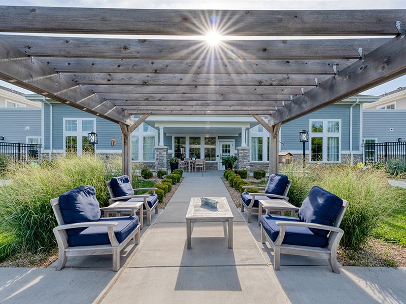 An inviting outdoor area at Cedarhurst of Yorkville, showing lush green spaces, paved paths, comfortable seating, a pergola, and a covered patio