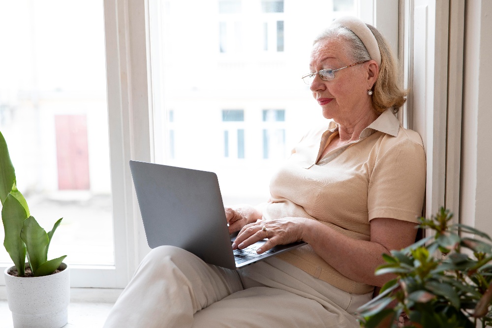 senior sitting in windowsill typing on a laptop
