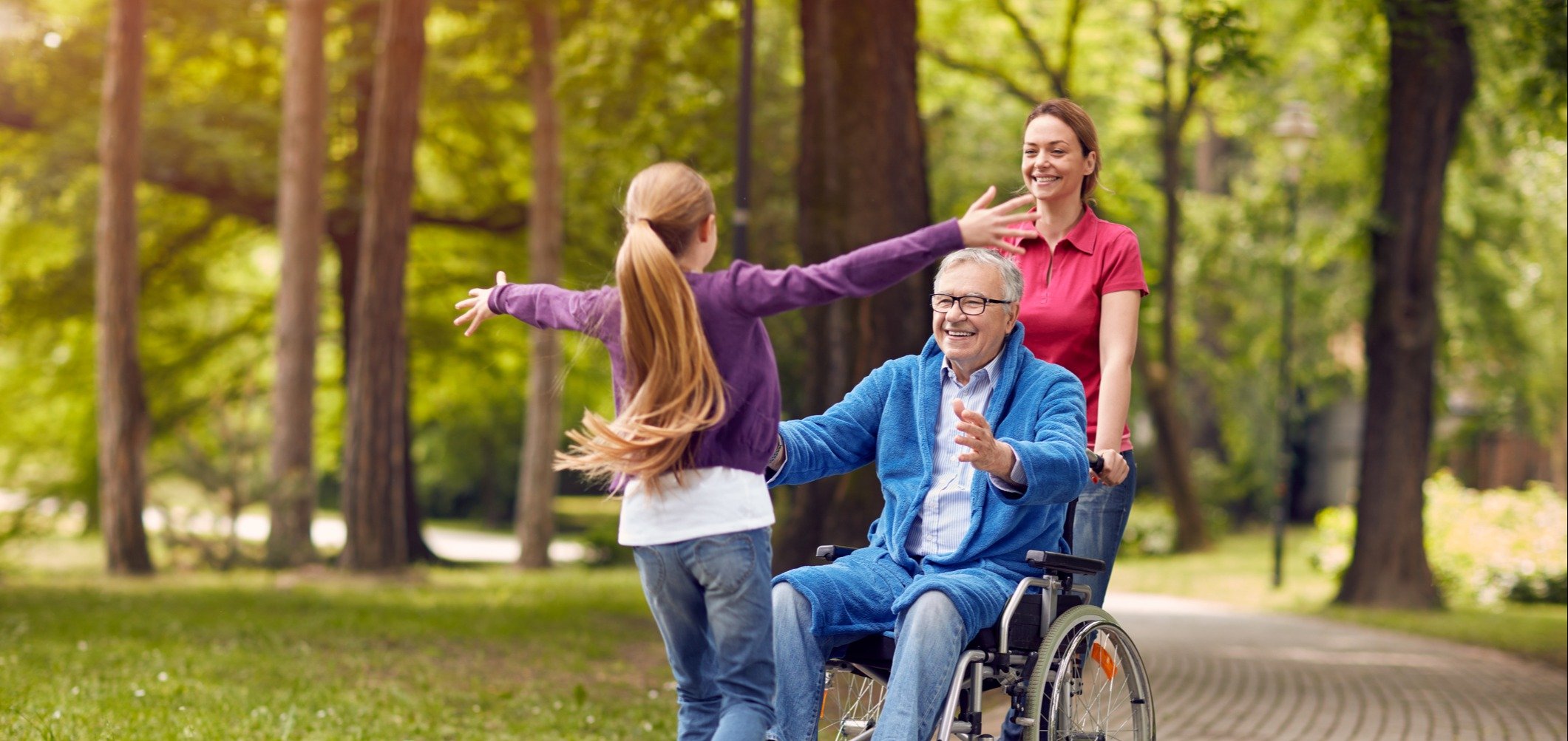 A team member pushes a senior resident in a wheelchair as he opens his arms to embrace his granddaughter running toward him