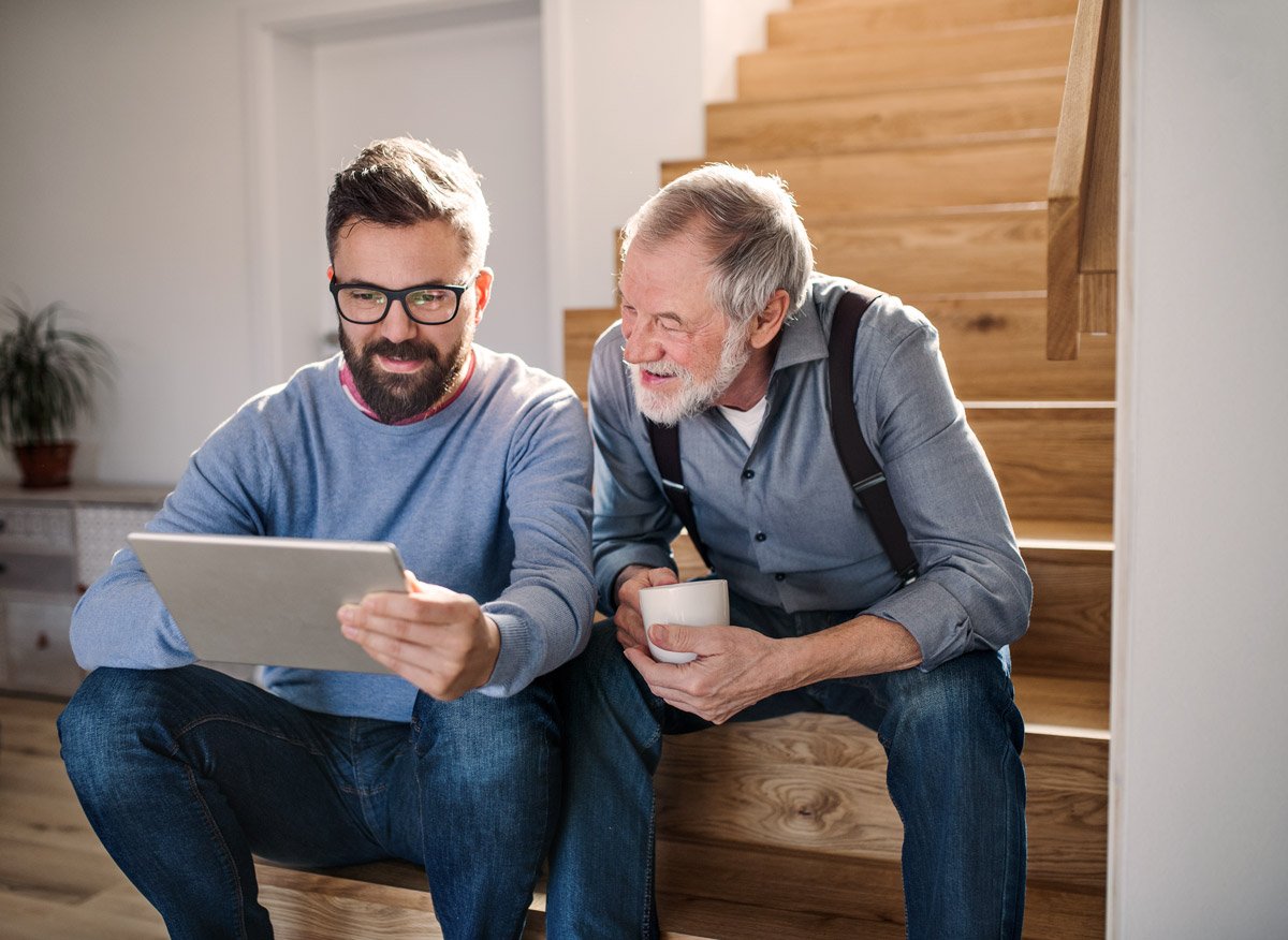 senior and son sitting on stairs looking at tablet