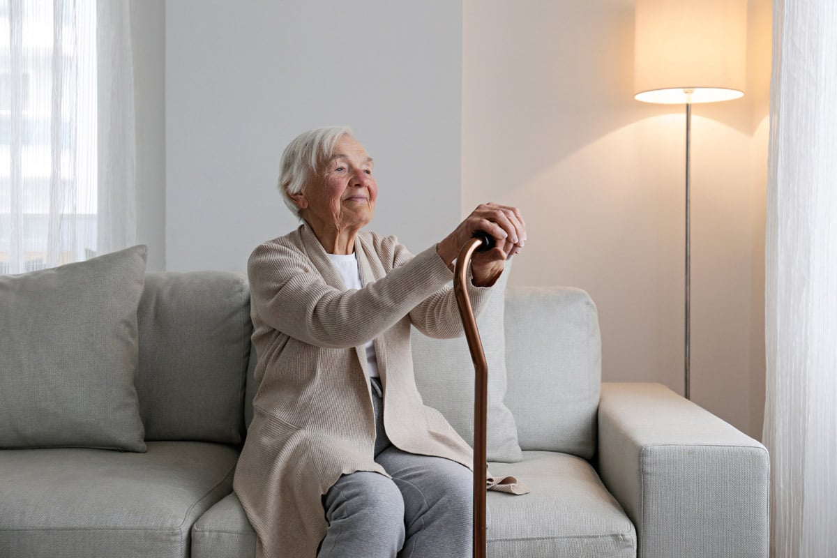 Senior sitting on couch, holding a walking cane