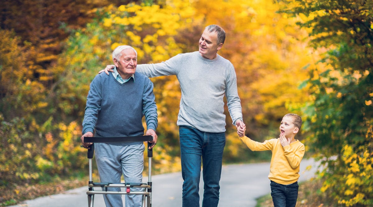 senior with a walker walking down paved trail with son and grandson