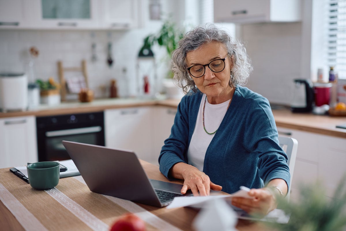senior woman working on finances with laptop in kitchen