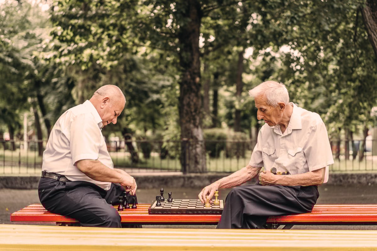 seniors playing chess outside on bench