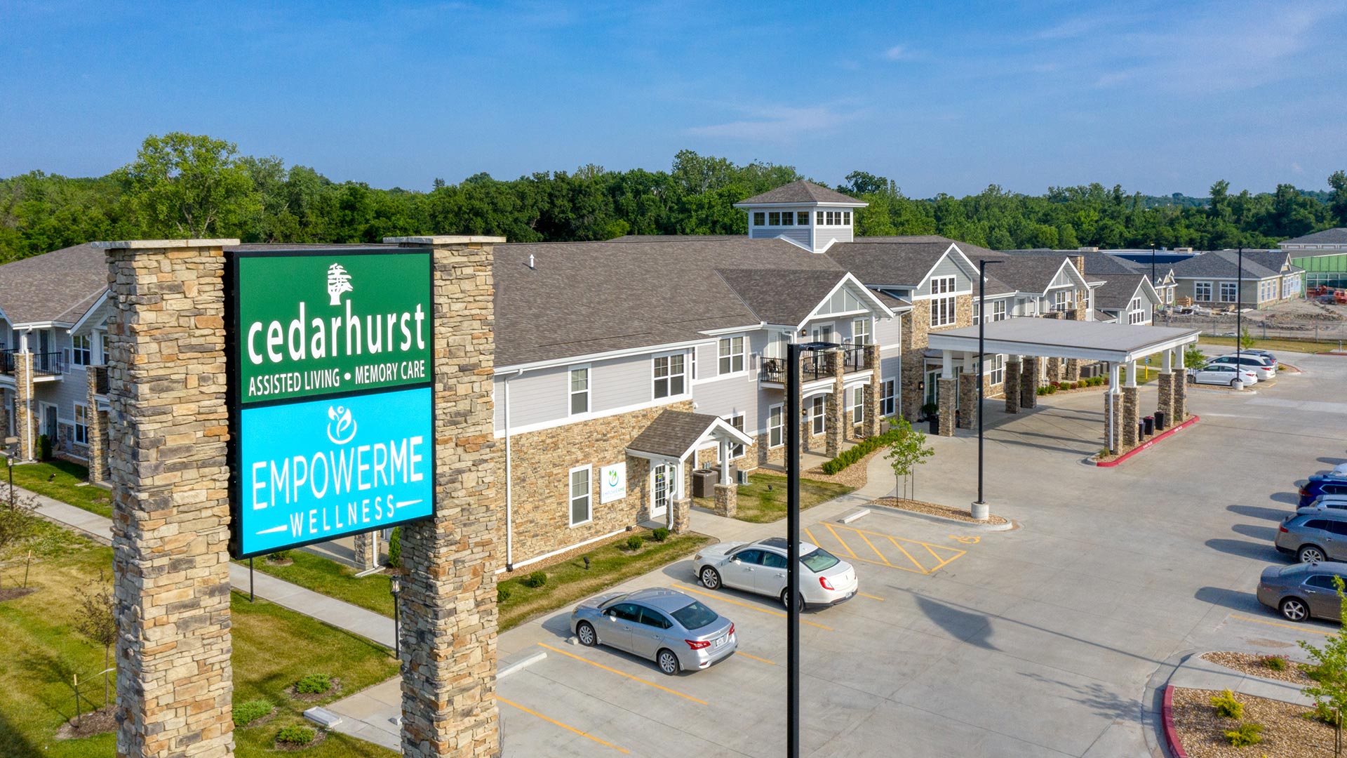 A modern,large, welcoming assisted living facility with a spacious parking area surrounded by greenery