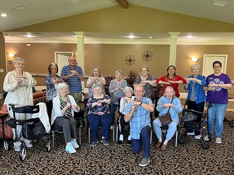 A group of seniors and adults smiling in a warmly lit community room copy