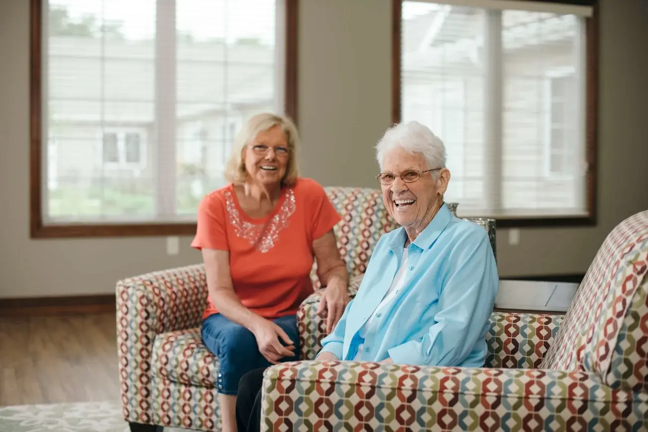 senior woman sitting with daughter on living room chairs