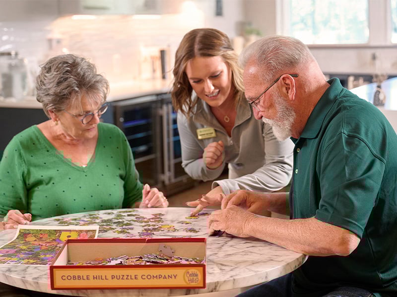 Senior living residents building a puzzle with the help of staff member