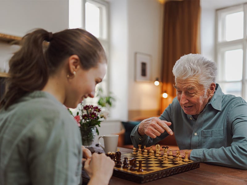 Senior living resident playing chess with staff member