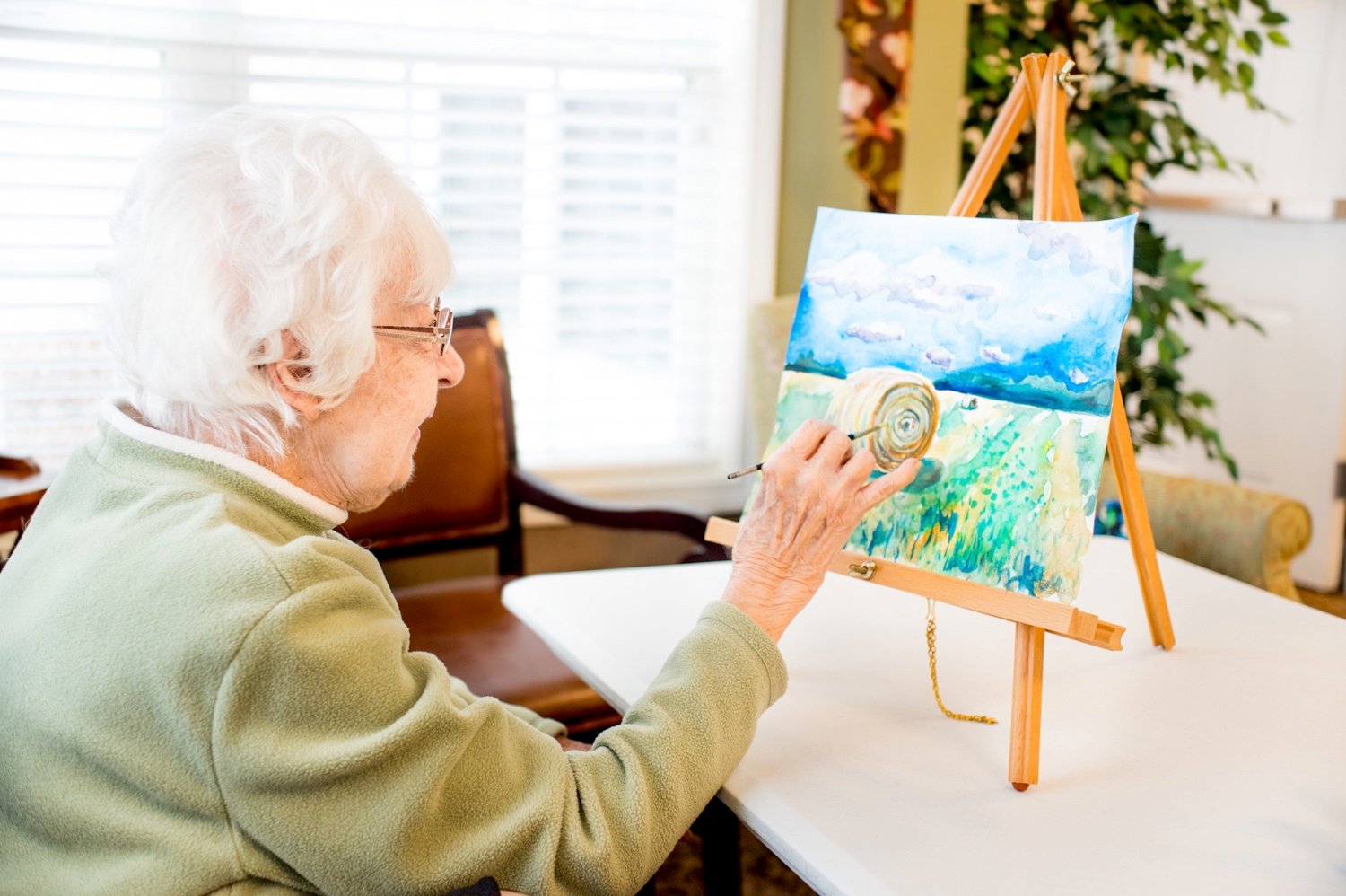 A senior woman painting a farm scene on an easel
