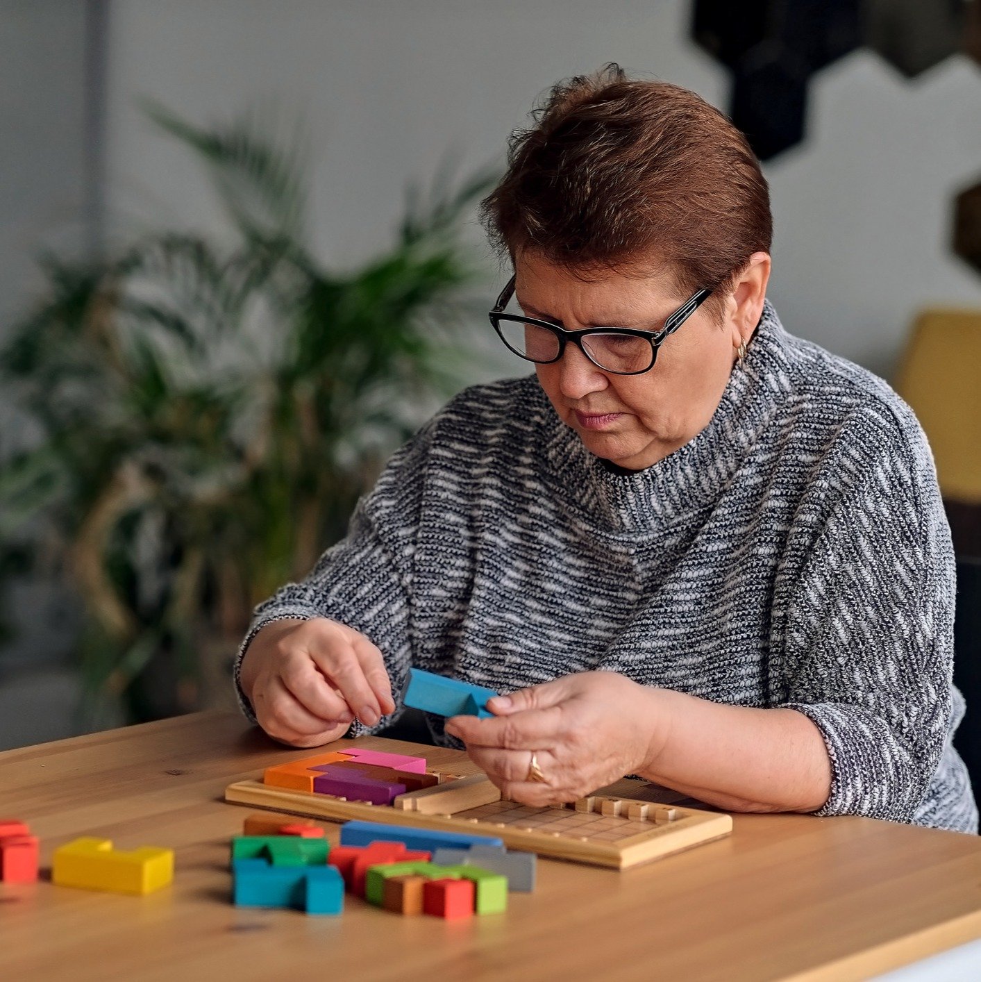 Elderly woman sitting at table and sorting jigsaw puzzle pieces