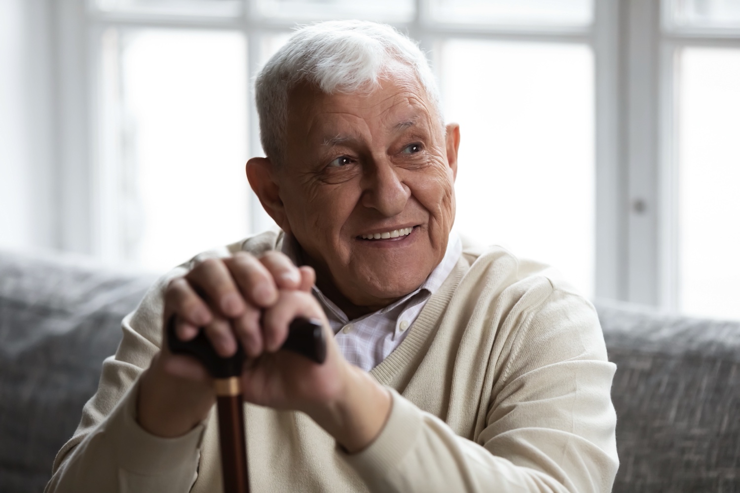 Senior man sitting on a couch and holding a walking cane