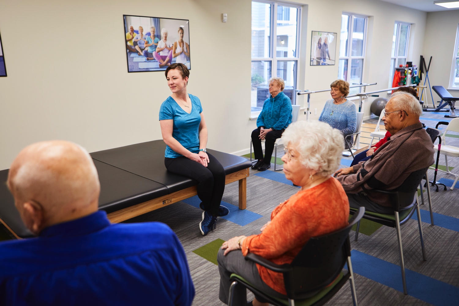 A group of seniors participating in a seated wellness class, following the guidance of a team member