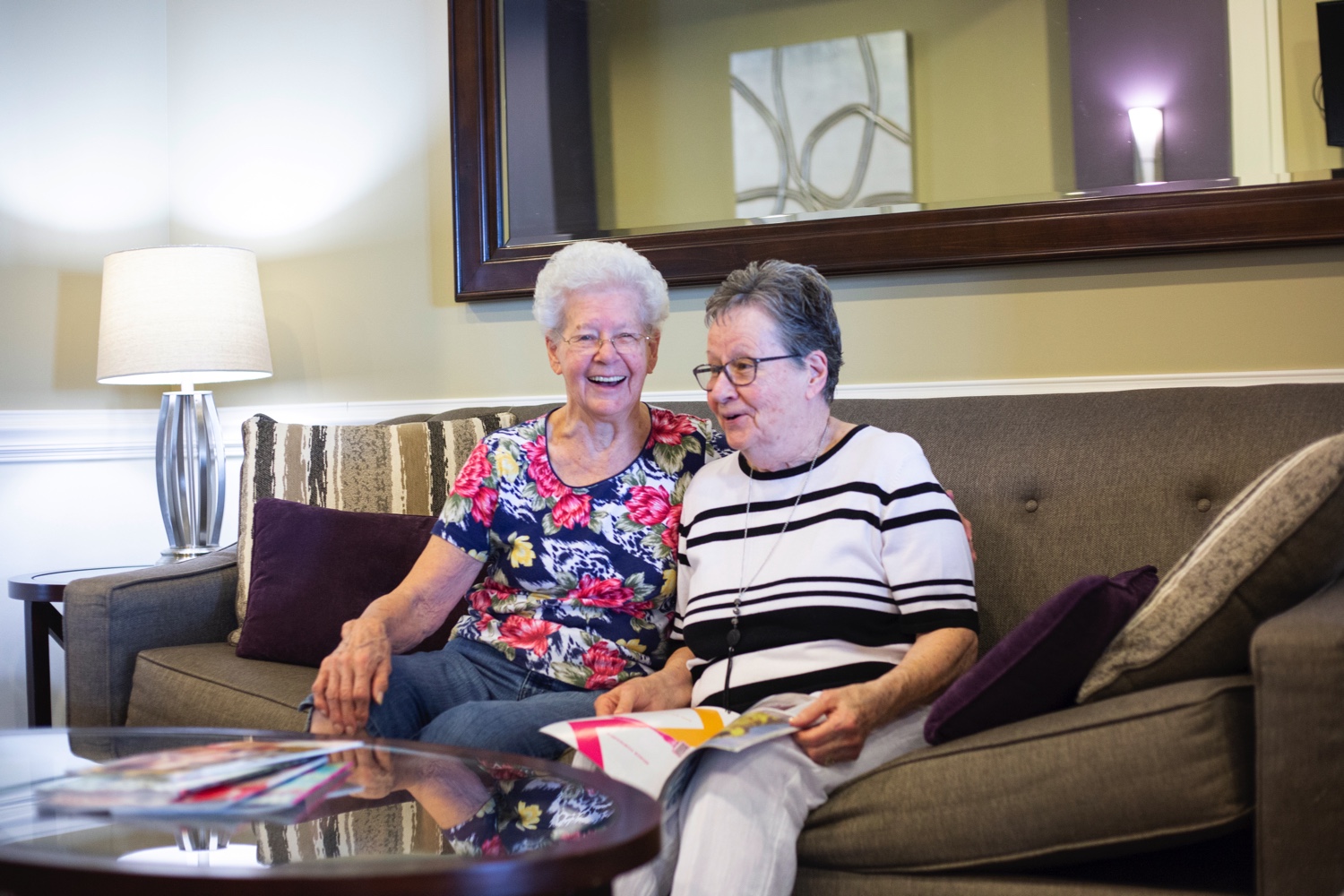 Two senior women Sitting on Couch Reading Magazine Together