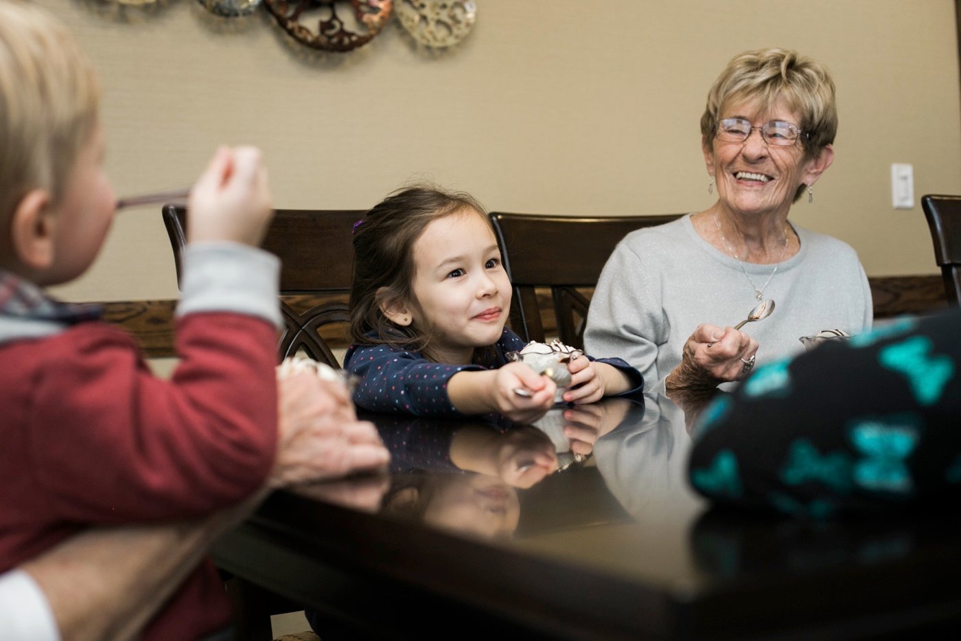 A grandmother eating ice cream with her grandchildren at a dining table