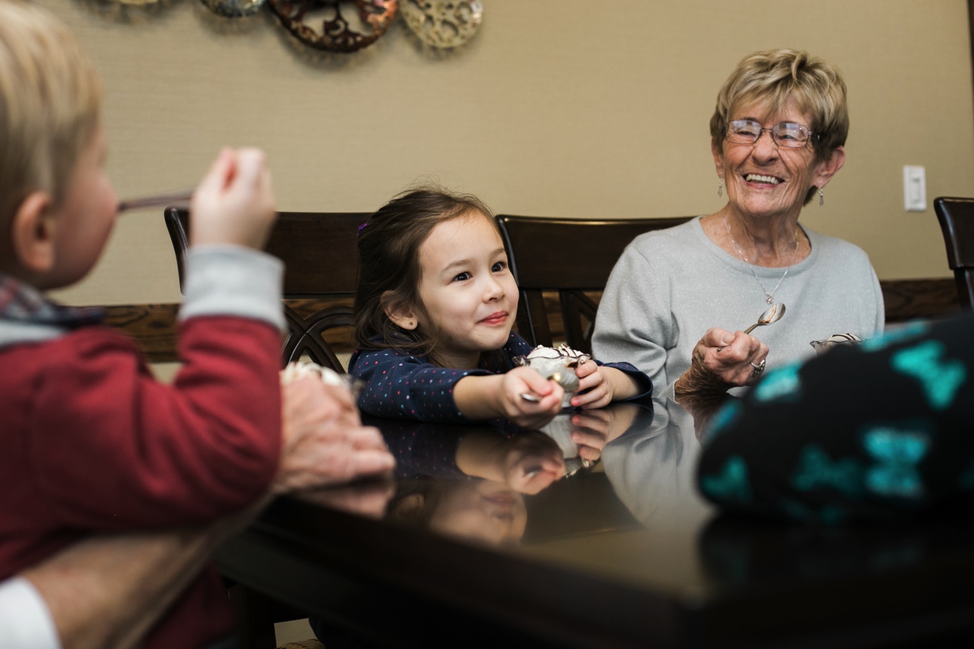 A grandmother eating ice cream with her grandchildren at a dining table