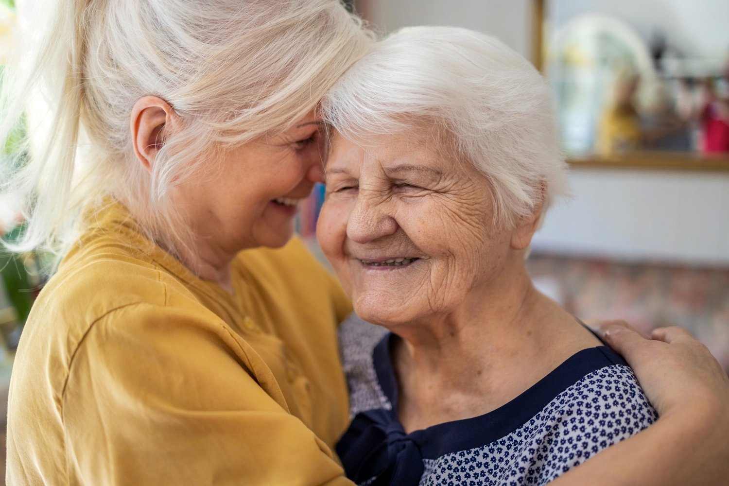 A senior woman smiling as she is embraced by another younger woman