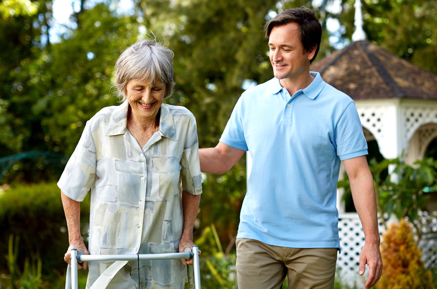 Carer helping senior with walker in garden