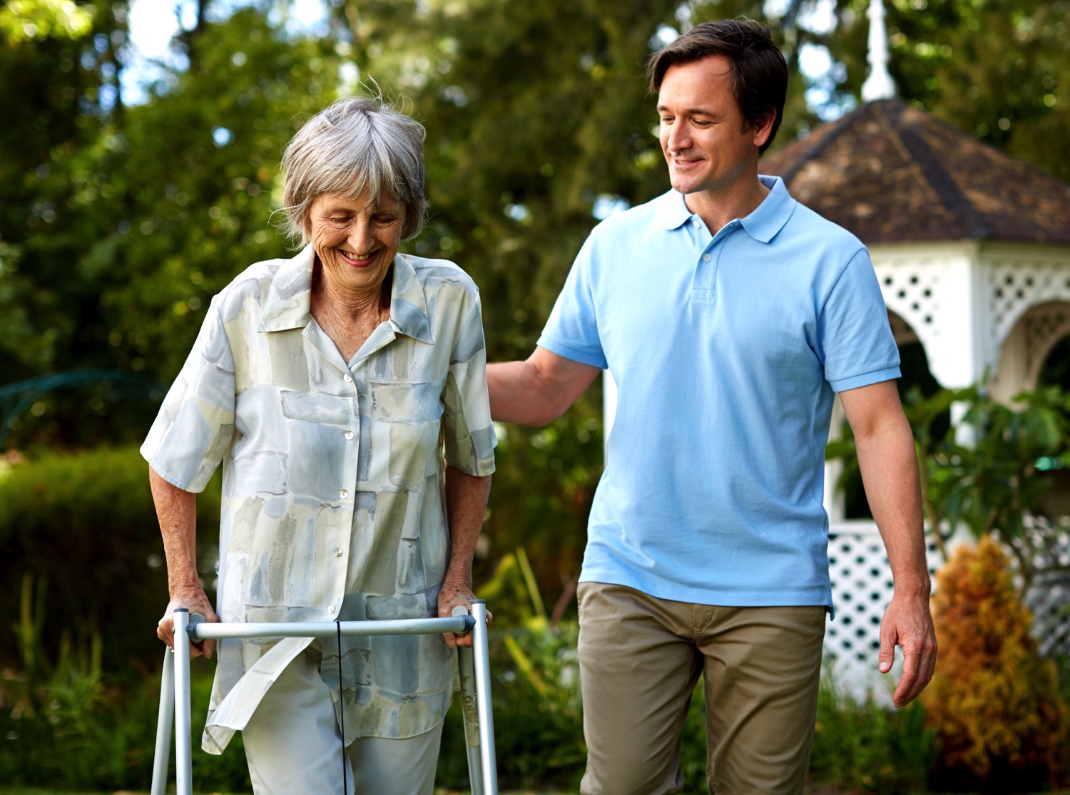 A staff member helping senior with walker in garden-1