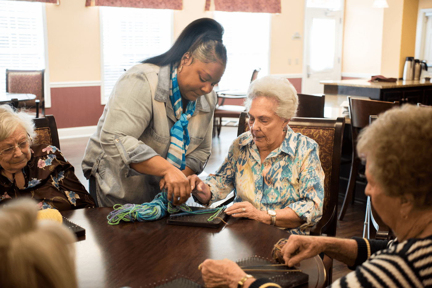 A team member helping a group of residents during a yarn craft activity