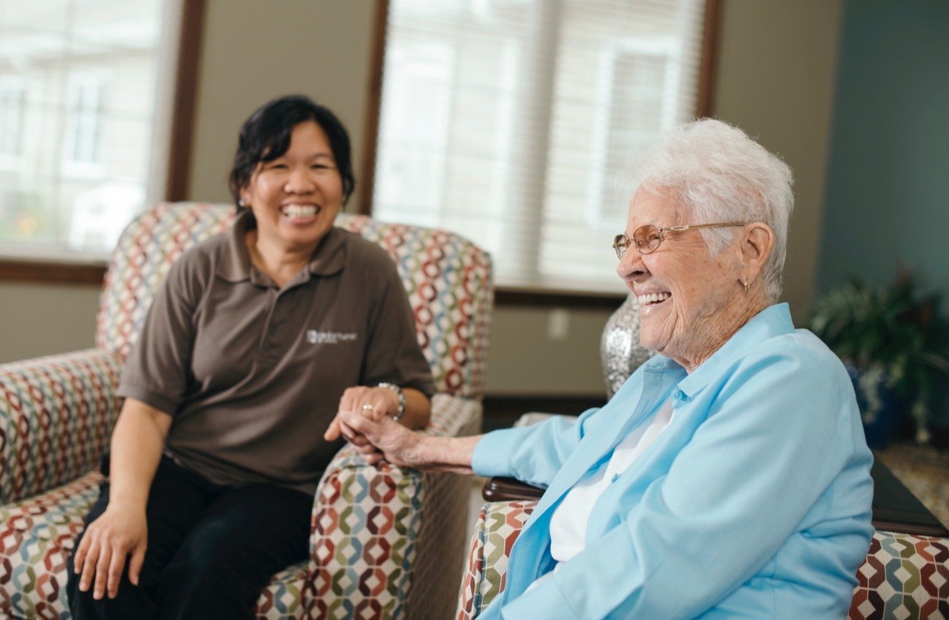 Cedarhurst staff member seated next to a resident, holding her hand