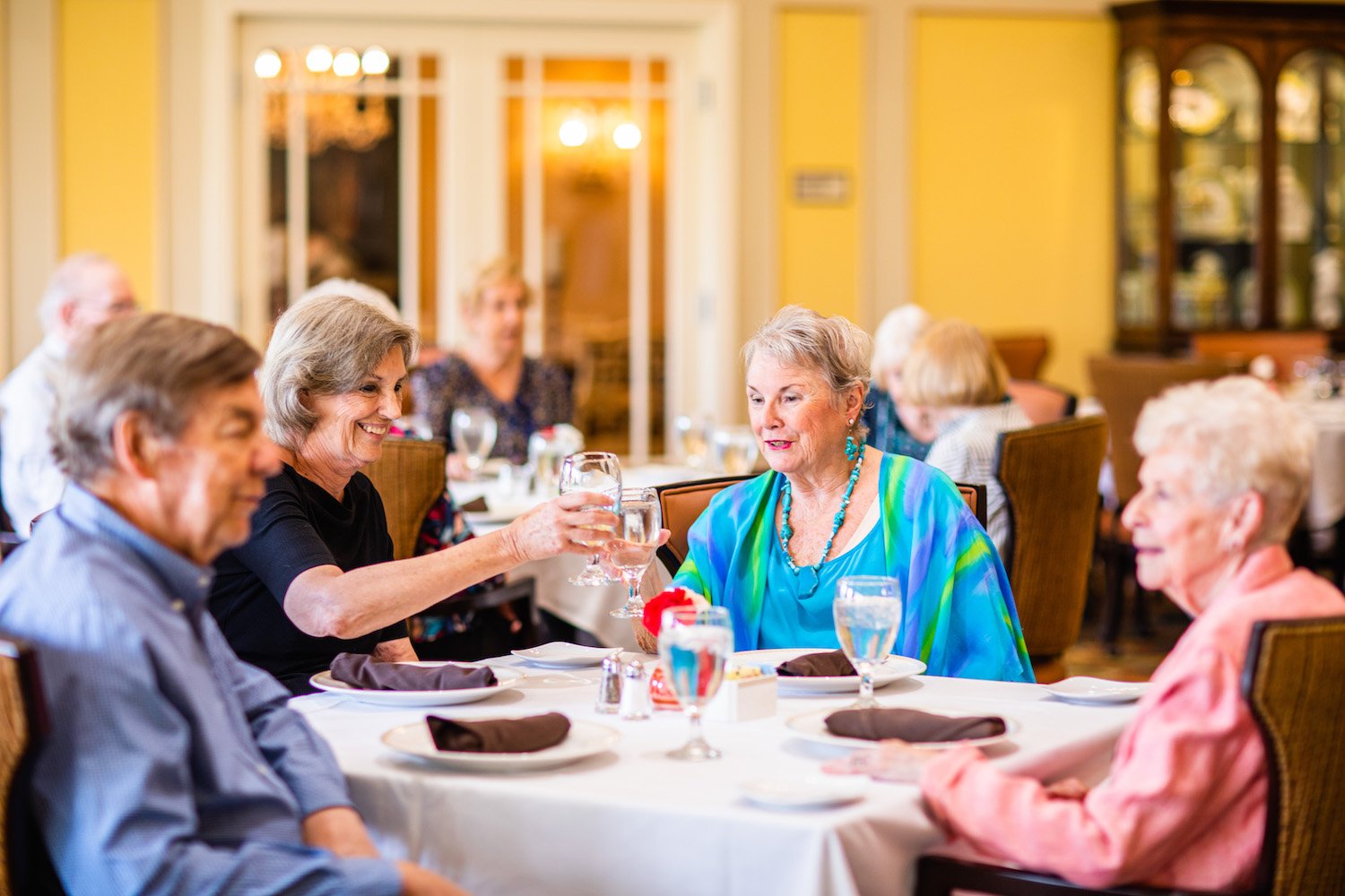 Senior women toasting with a drink at a dining table