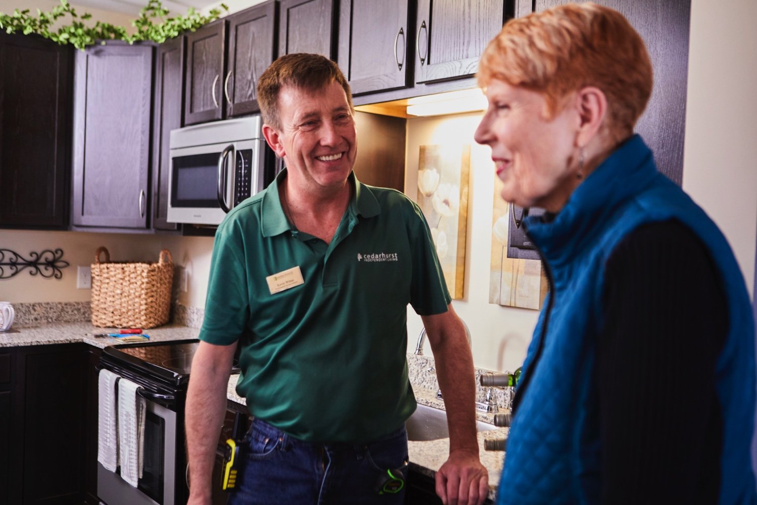 A staff maintenance man laughing with a senior resident in her kitchen