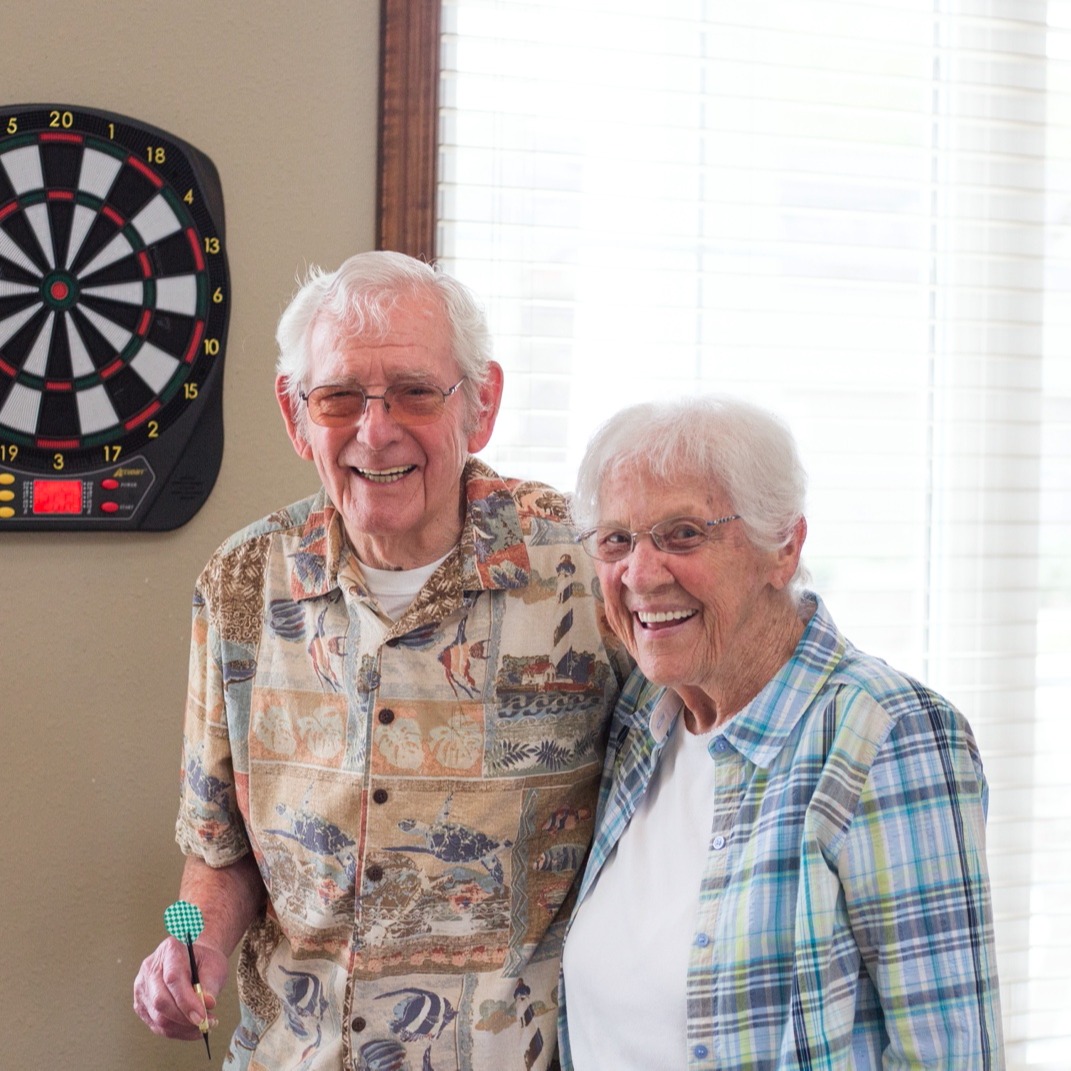 A resident couple smiling and playing darts